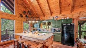 Cocina de cabaña de madera con una isla central, gabinetes verdes y un refrigerador negro.