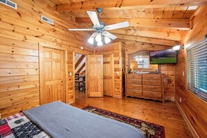 A wooden cabin bedroom with a bed, dresser, and ceiling fan.