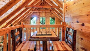 Un comedor de madera con mesa y sillas, techo inclinado y ventanas con vistas a la vegetación.