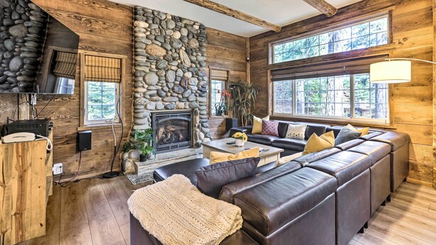A log cabin interior with a stone fireplace, wooden walls, a leather sofa, and large windows. - 6 Mi to Homewood Mountain Resort: Tahoe City Gem! (Tahoe City)