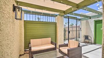 Un patio al aire libre con mobiliario de mimbre, una puerta verde y una reja de metal.