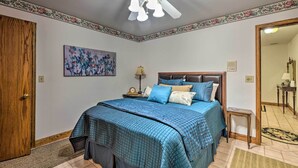 A bedroom with a bed, a ceiling fan, a nightstand, a lamp, and a painting on the wall. - Pet-friendly Home 7 Miles to Dickson Street! (Fayetteville)