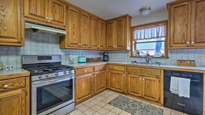 A kitchen with wooden cabinets, a stainless steel stove, a dishwasher, and a window with a curtain. - Pet-friendly Home 7 Miles to Dickson Street! (Fayetteville)