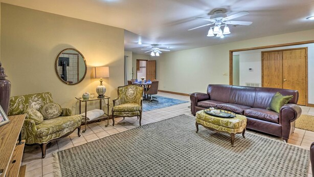 A living room with a brown leather sofa, a green patterned armchair, a small round table with a lamp, and a coffee table. - Pet-friendly Home 7 Miles to Dickson Street! (Fayetteville)