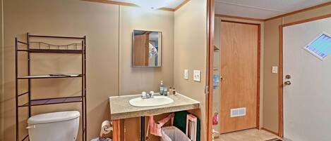 A compact bathroom with a toilet, sink, and shelving unit.