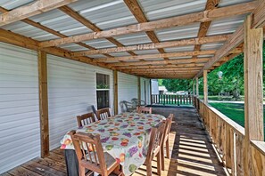 A covered outdoor patio with a wooden table and chairs, a metal roof, and a view of a green yard.