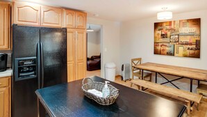 A kitchen with wooden cabinets, a black refrigerator, a coffee maker, a sink, and a dining table with benches.
