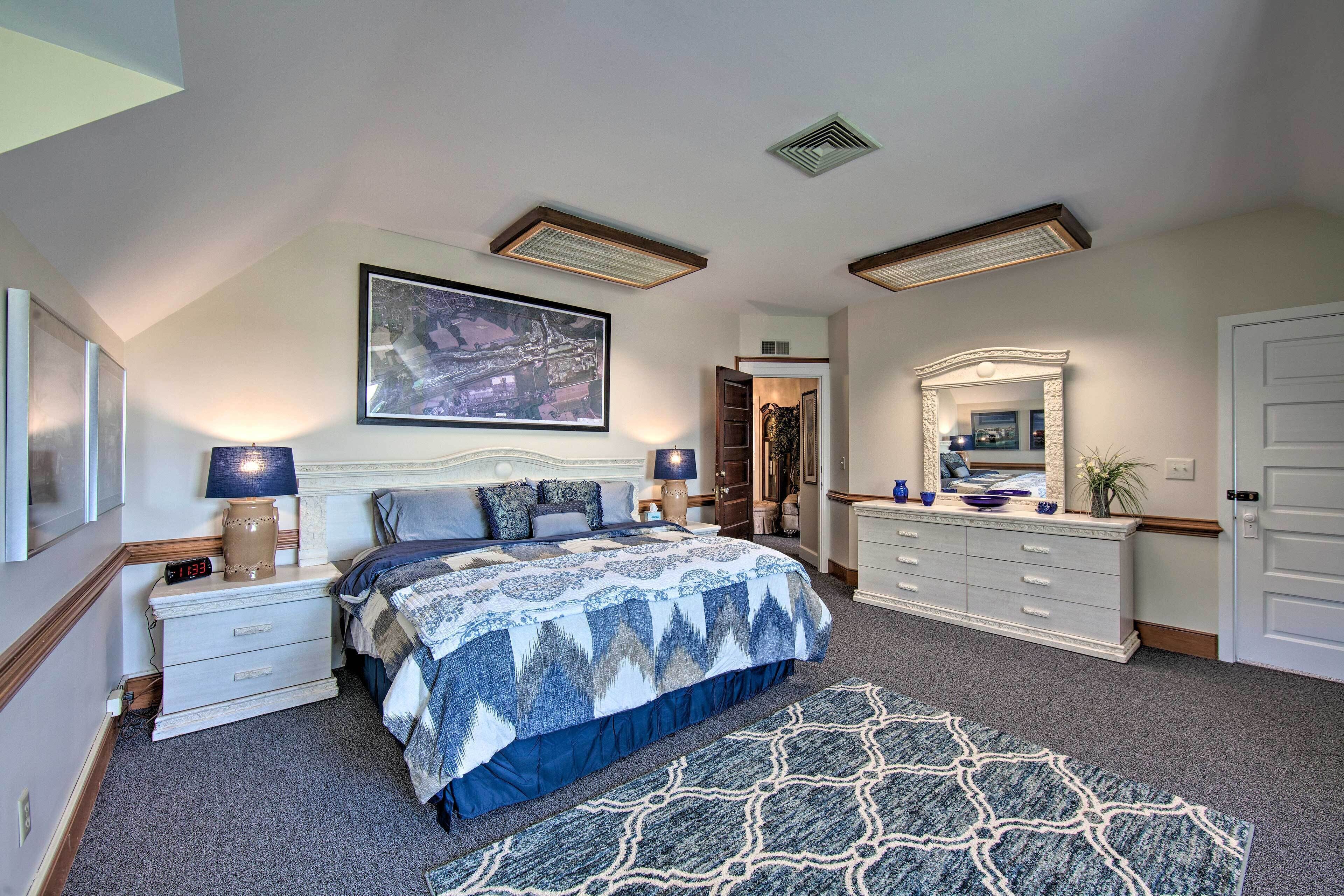 A bedroom with a bed, bedside tables, a dresser, a mirror, and a painting on the wall.