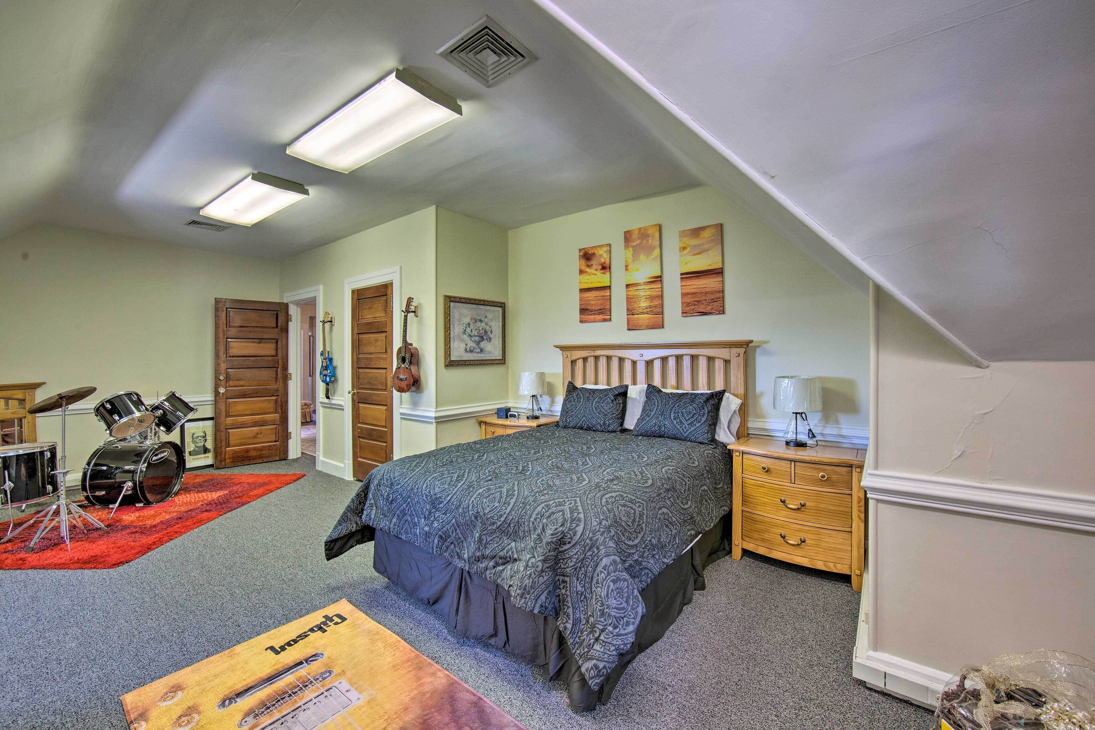 Une chambre à coucher avec un lit, des tables de chevet, une commode, une guitare et une batterie.