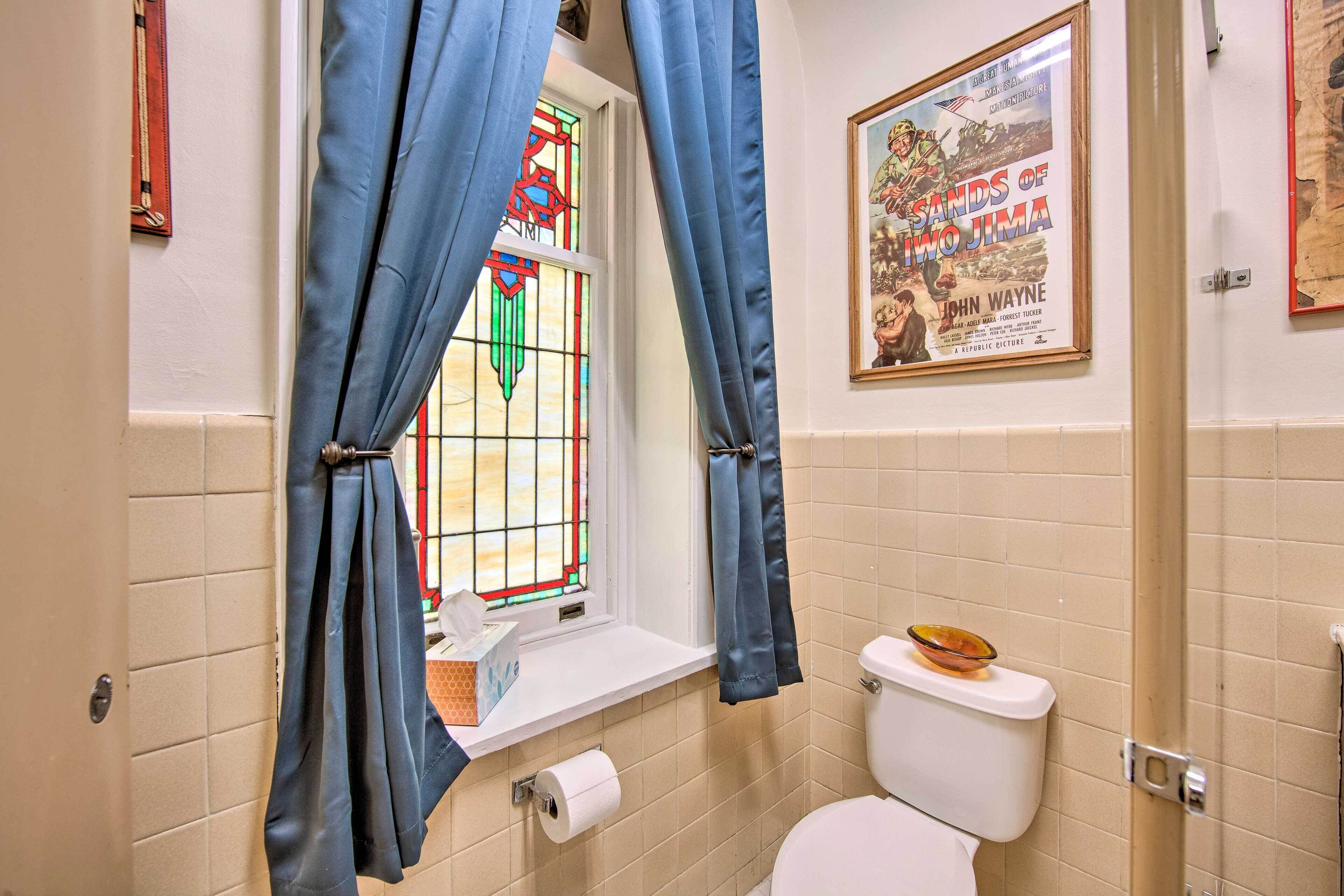 A bathroom with a toilet, a roll of toilet paper, a small shelf, and a poster on the wall.