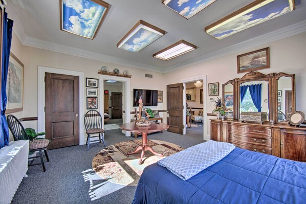 Una habitación con cama, escritorio, sillas, cómoda y un techo con tragaluces.