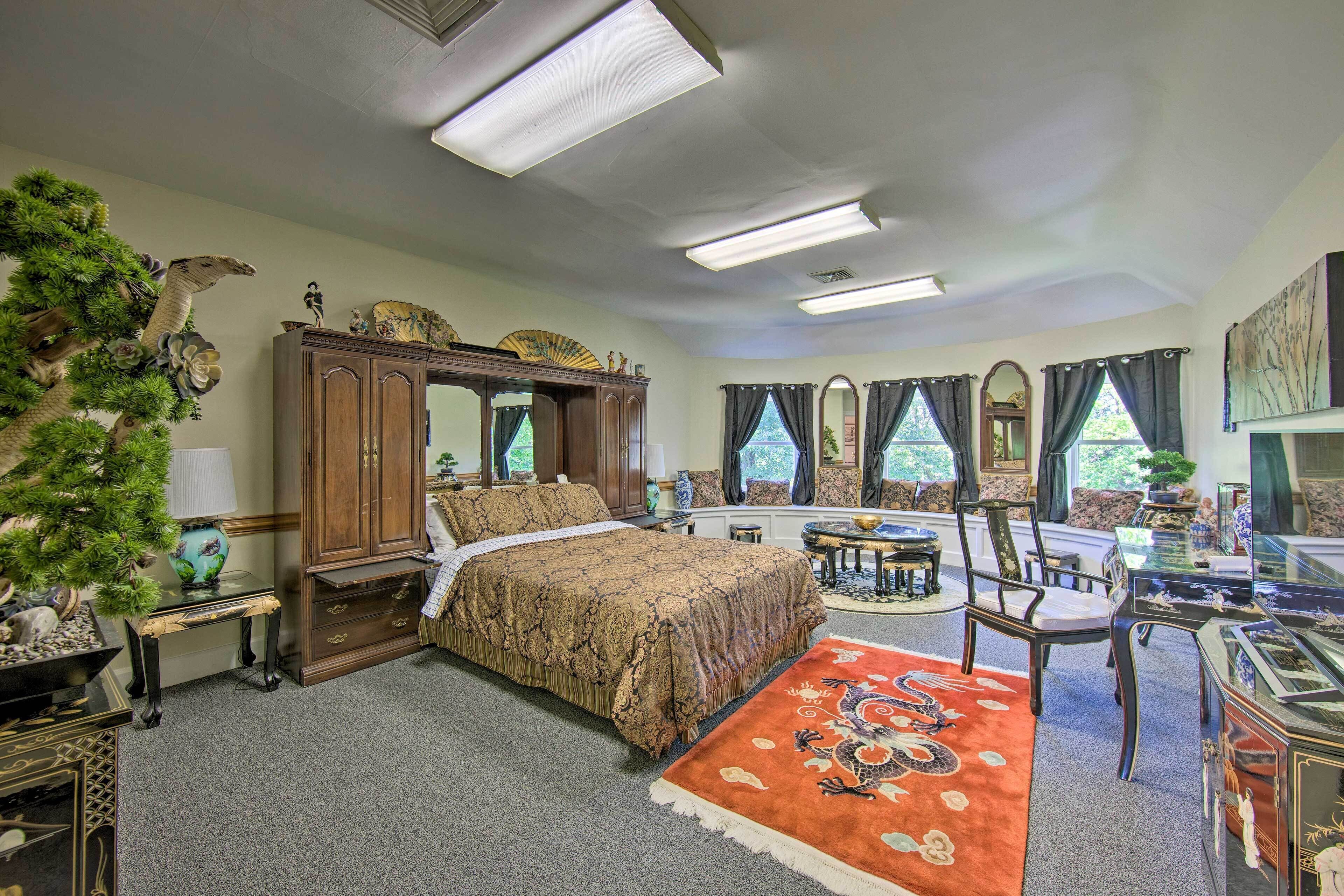 A bedroom with a bed, a desk, and a chair. There is a window with curtains, a dresser, and a lamp.