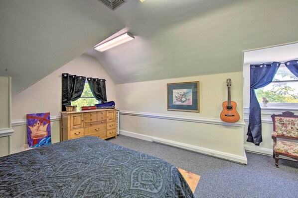 A bedroom with a bed, dresser, guitar, and artwork.