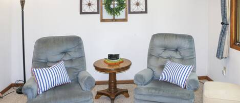 Dos sillones grises con almohadones a rayas, una mesita de madera con un adorno, y un otoman blanco.