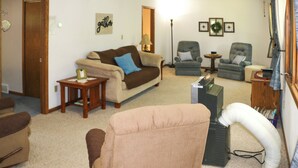 A living room with a beige sofa, a brown armchair, and a grey armchair. There is a lamp, a small table, and a vacuum cleaner. - Fishermen's Paradise w/ Fire Pit on Rice Lake! (Rice Lake)