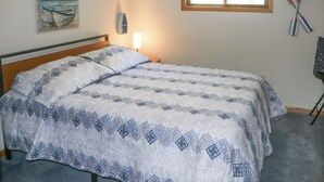 A bedroom with a bed, a nightstand, a wall-mounted lamp, a window, and a painting. - Fishermen's Paradise w/ Fire Pit on Rice Lake! (Rice Lake)