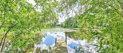 A wooden dock extending into a calm body of water surrounded by lush greenery.