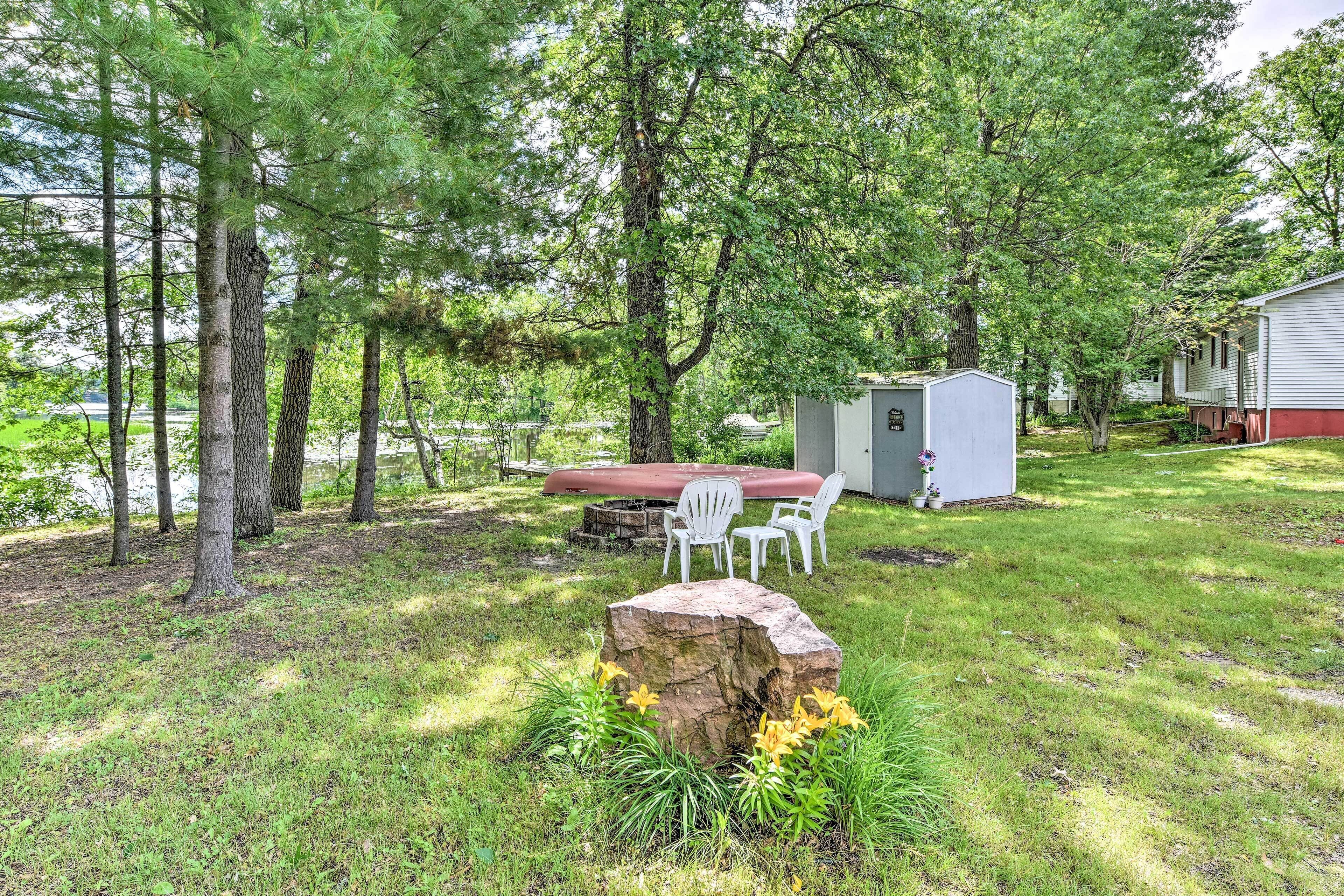 Un espacio al aire libre con césped, una mesa de picnic y sillas, una roca grande y un cobertizo pequeño.