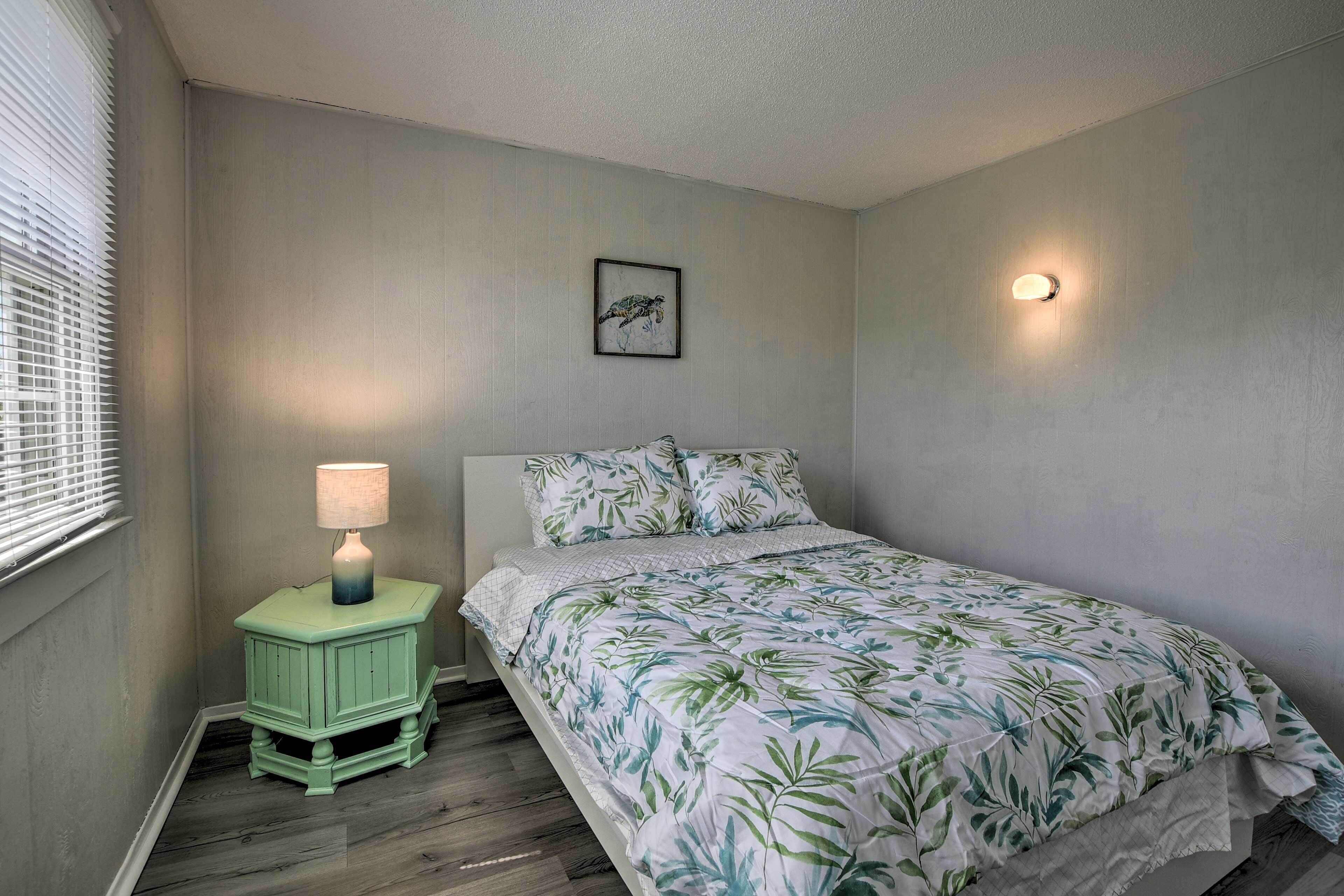 A bedroom with a bed, a nightstand with a lamp, a framed picture on the wall, and a wall-mounted light.