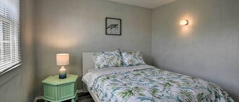 A bedroom with a bed, a nightstand with a lamp, a framed picture on the wall, and a wall-mounted light.