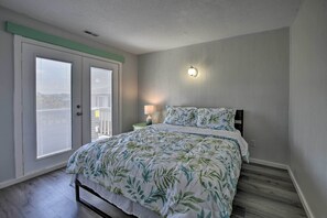 A bedroom with a bed, a nightstand, a lamp, and a wall-mounted light fixture. - Oak Island Beach Abode w/ Deck: Walk to Shore! (Oak Island)