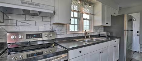 A modern kitchen with white cabinets, stainless steel appliances, a double sink, and a window with blinds.