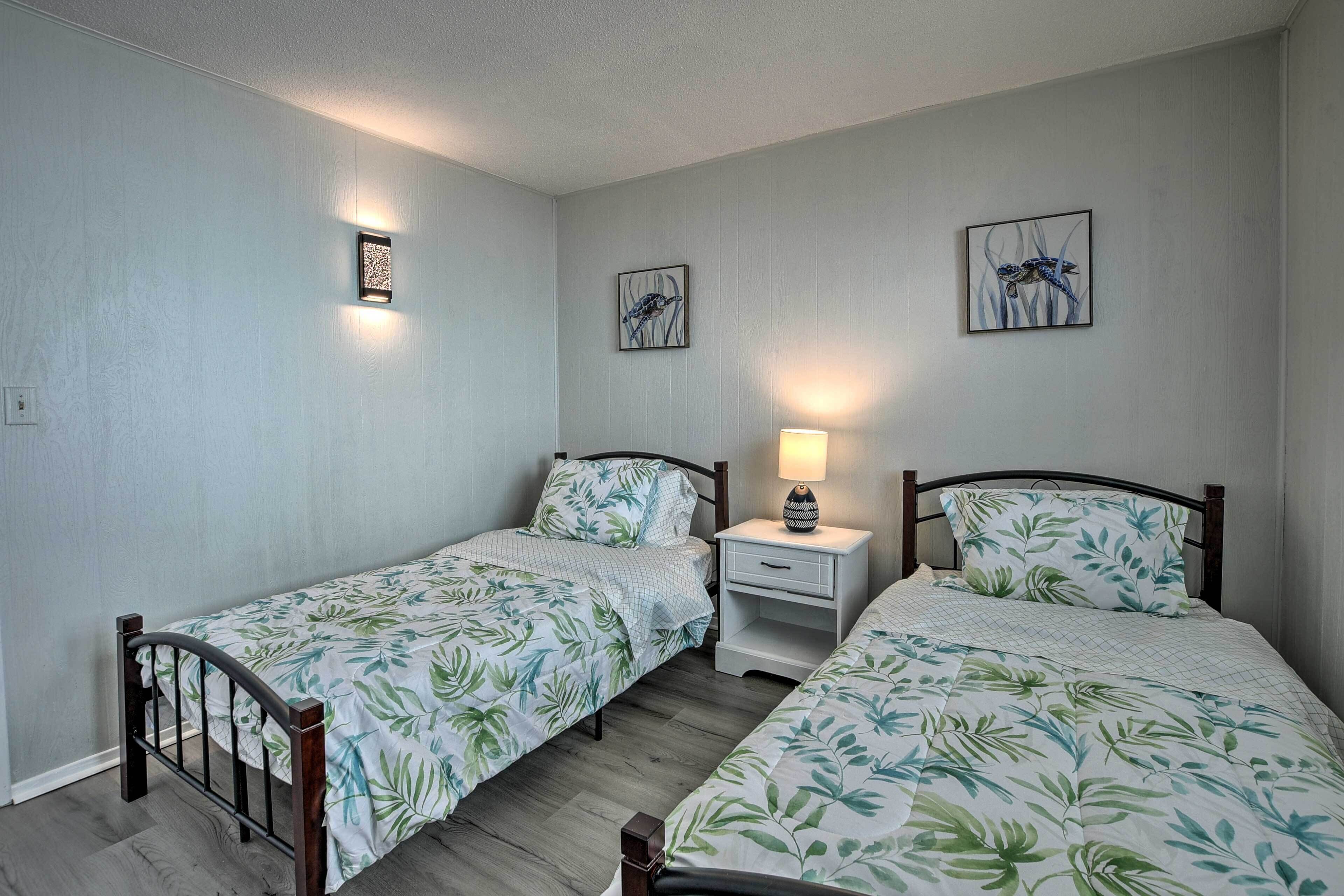 Une chambre avec deux lits simples, une table de chevet avec une lampe et des œuvres d’art accrochées au mur.