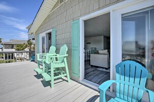 Una terraza techada con sillas Adirondack turquesa y una puerta corrediza que da a un cuarto con una cama y una mesita.