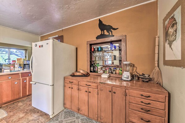 Uma cozinha com geladeira, armários de madeira, uma prateleira de vidro com utensílios de cozinha e uma placa fixada na parede.