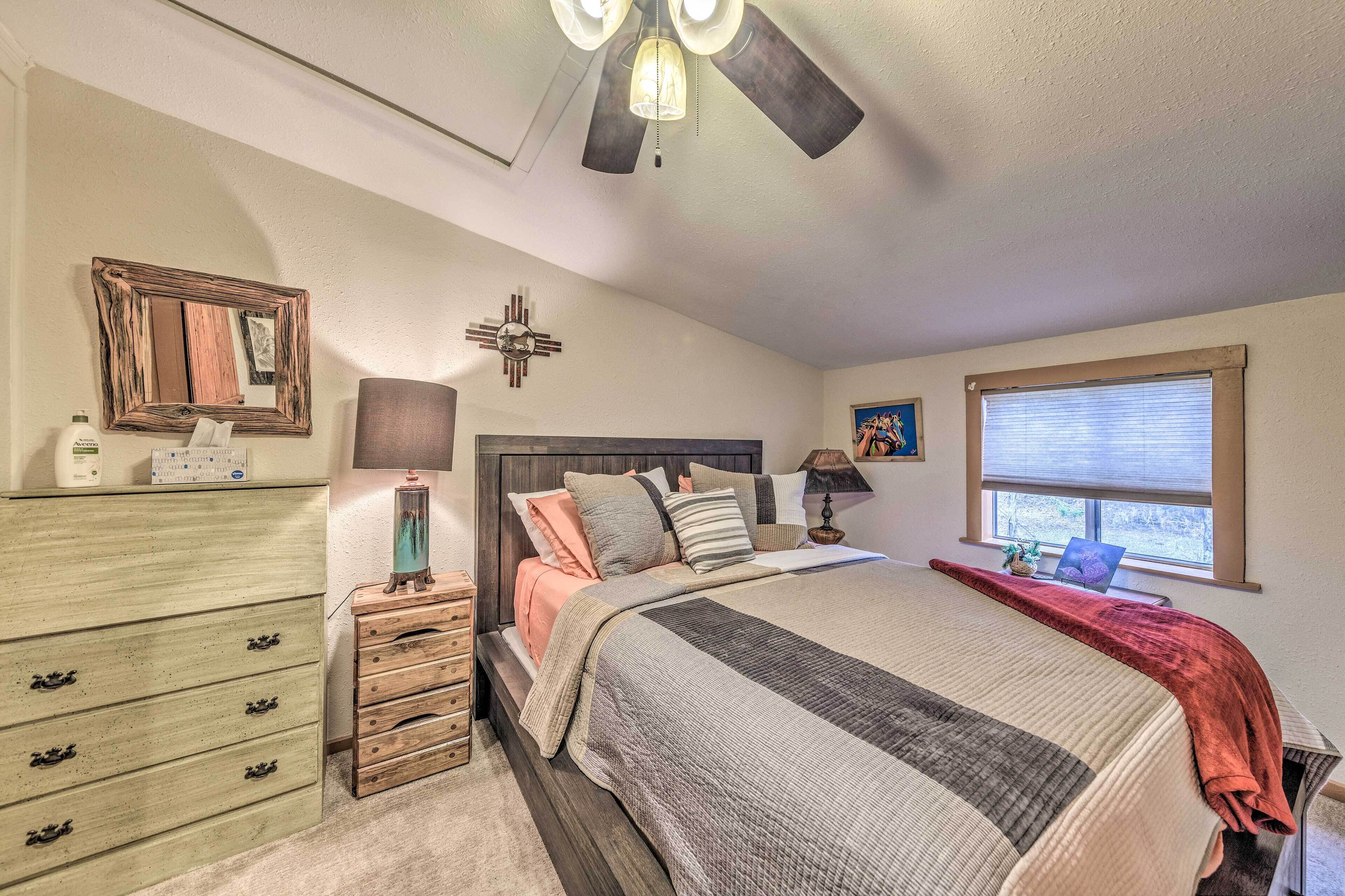 A bedroom with a bed, dresser, nightstand, ceiling fan, window, and wall decor.