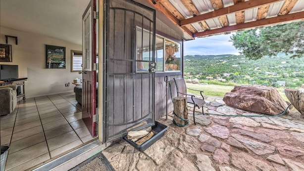 A cozy living area with a stone floor, a wooden door leading outside, and a view of a lush landscape. - Cozy High Rolls Cottage Near Hiking Trails! (High Rolls Mountain Park)