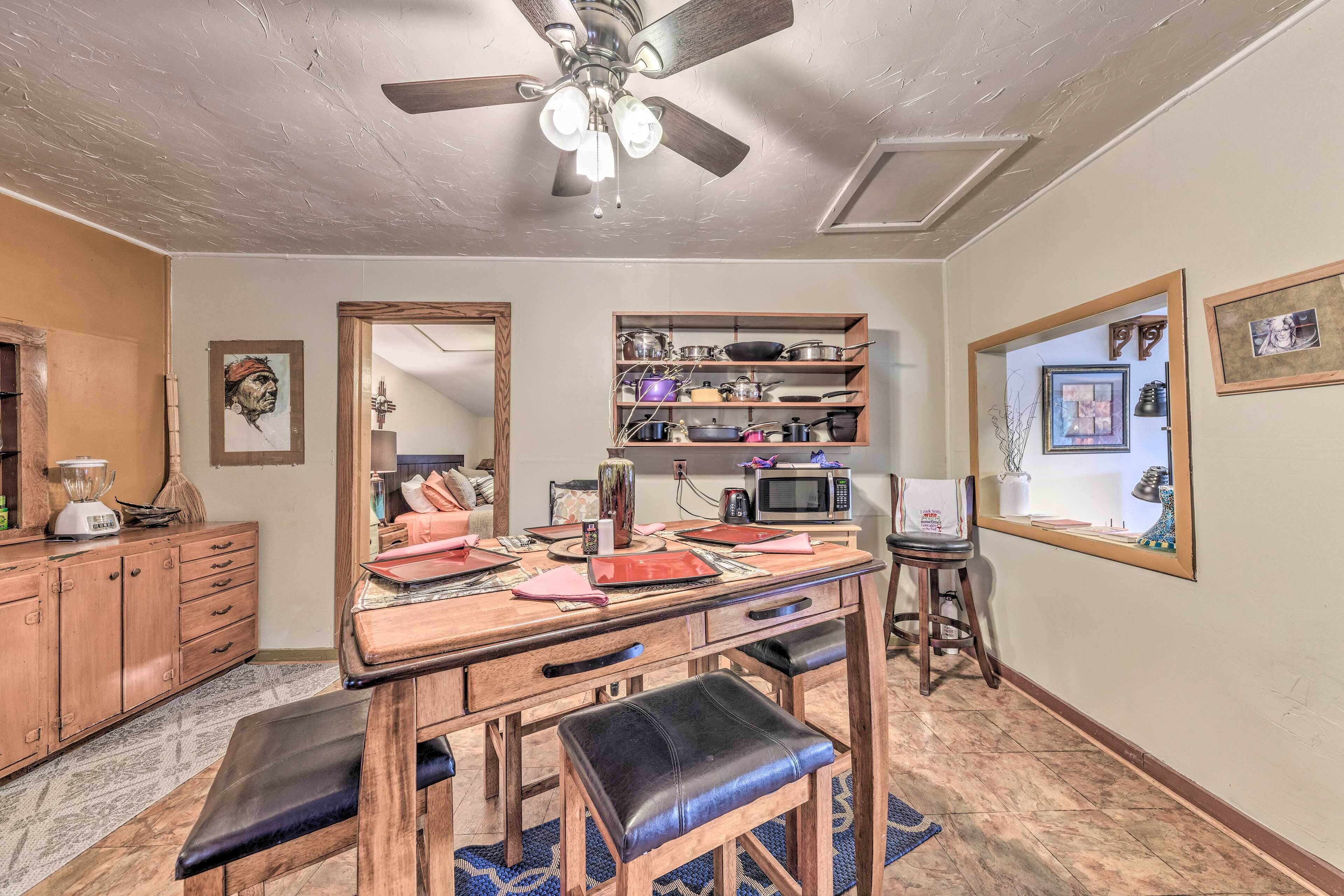 A kitchen with a wooden table, stools, a ceiling fan, and a microwave.