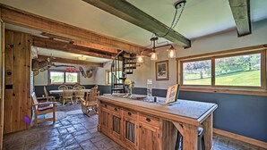 A rustic kitchen with wooden cabinets, a central island, and a dining area with wooden chairs.