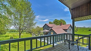 A wooden deck with a railing overlooking a grassy field and a house with a red roof.