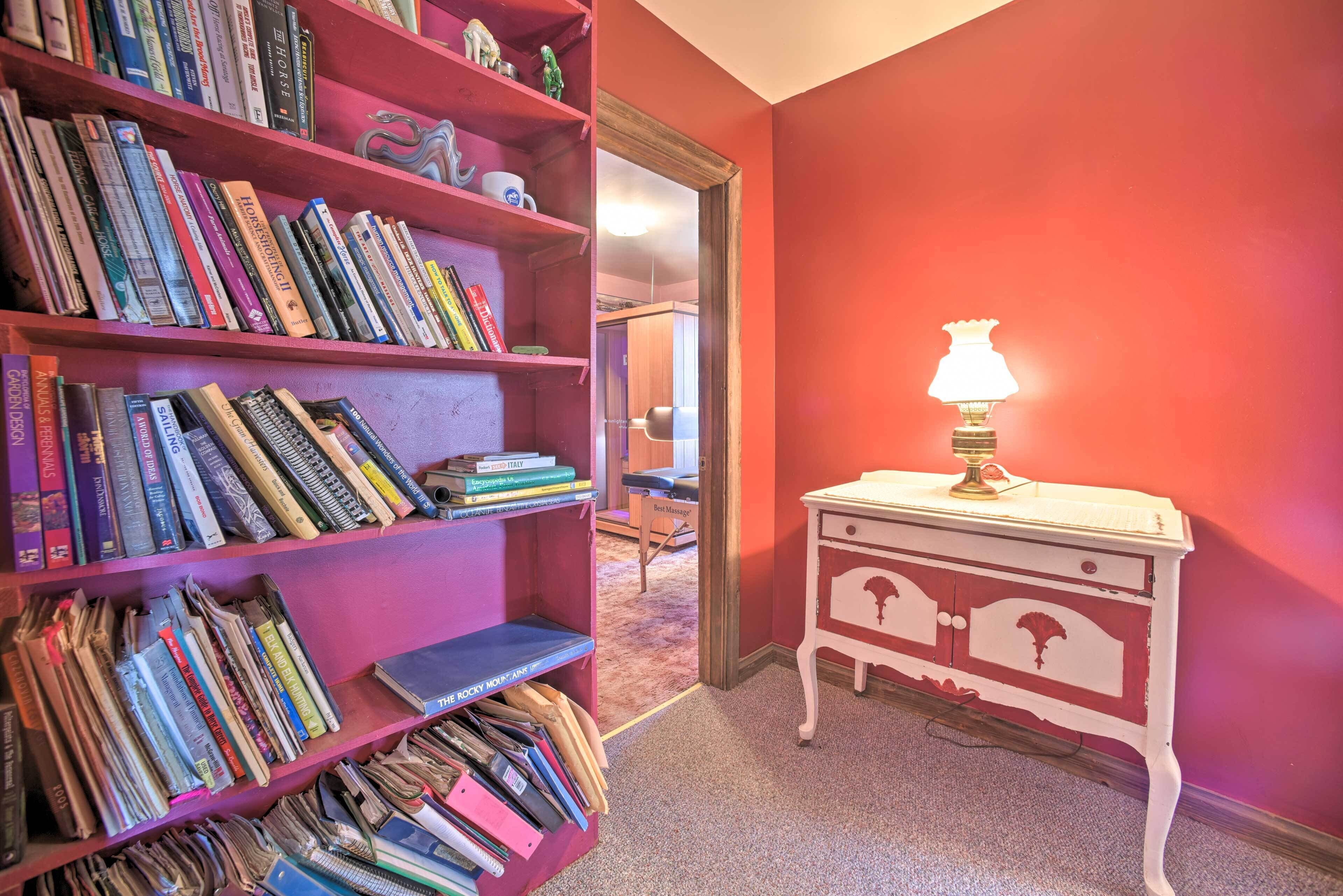 Una stanza con una libreria piena di libri, un comò bianco con una lampada e un muro rosso.