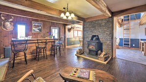 A rustic interior with a stone fireplace, wooden beams, a bar area, and a deer head decoration.