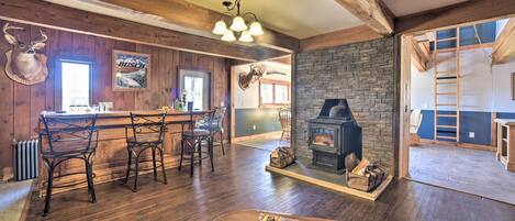 Un interior rústico con chimenea de piedra, vigas de madera, una zona de bar y una decoración con cabeza de venado.