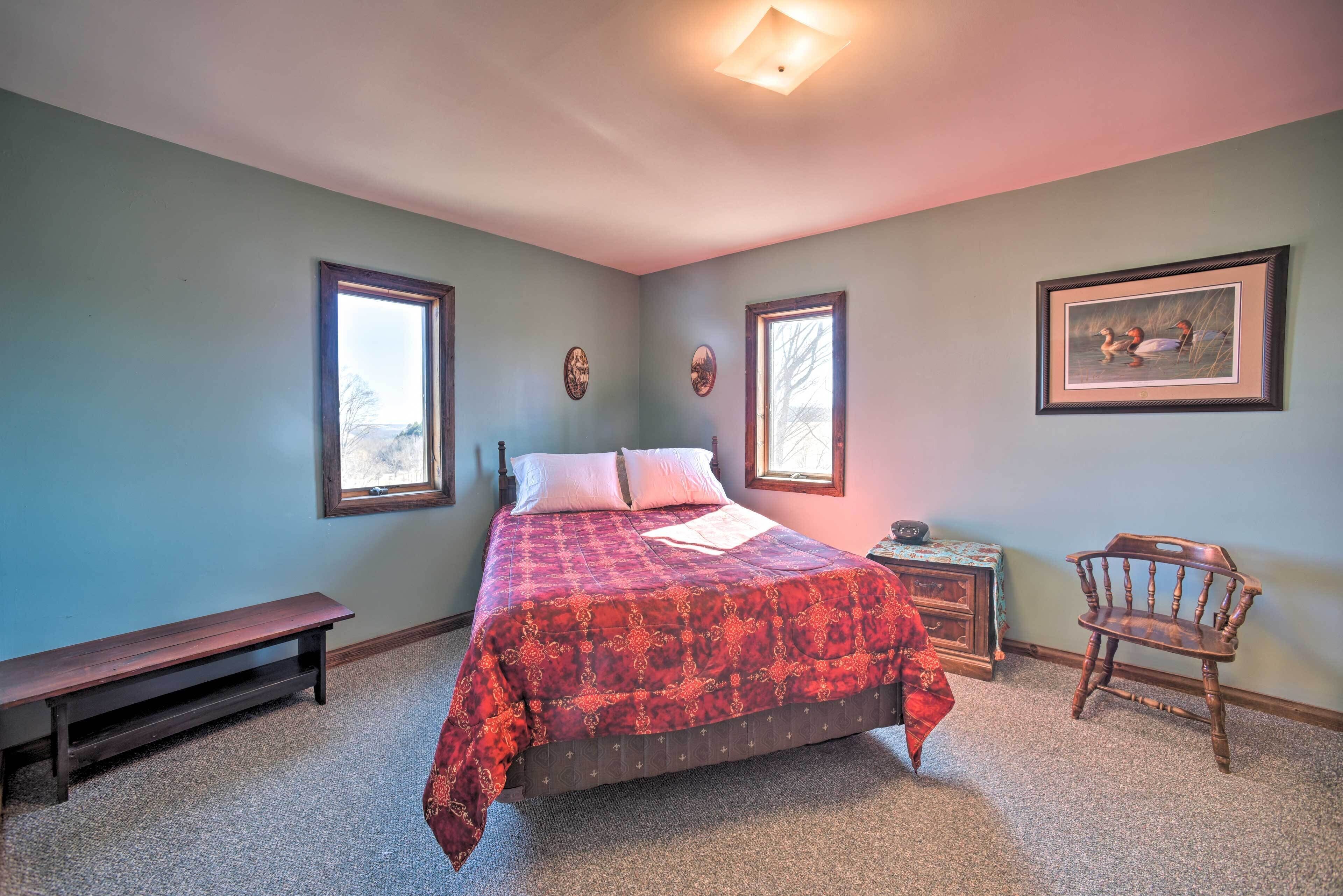 A bedroom with a bed, a bench, a chair, and two framed pictures on the wall.