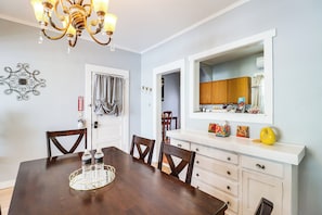 A dining area with a wooden table, chairs, a chandelier, a fire extinguisher, and a kitchen area with cabinets and a mirror. - 'St Blaise' Bisbee Apt < 1 Mi to Attractions! (Bisbee)
