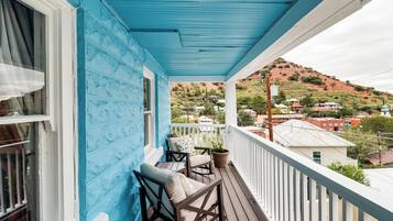 A balcony with a blue exterior, wooden furniture, and a view of a hilly landscape.