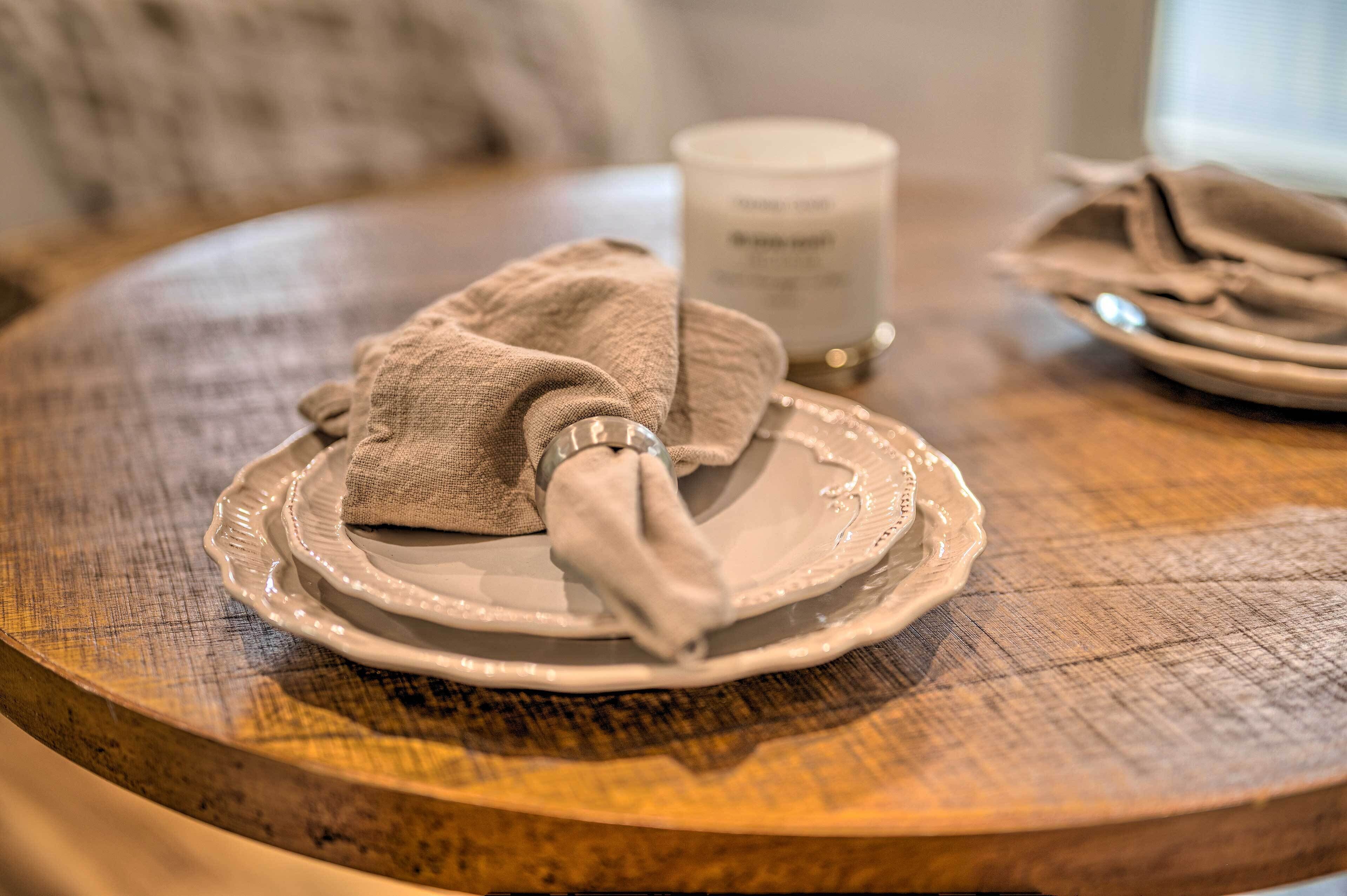 A round wooden table with a white plate, a folded napkin, and a candle.