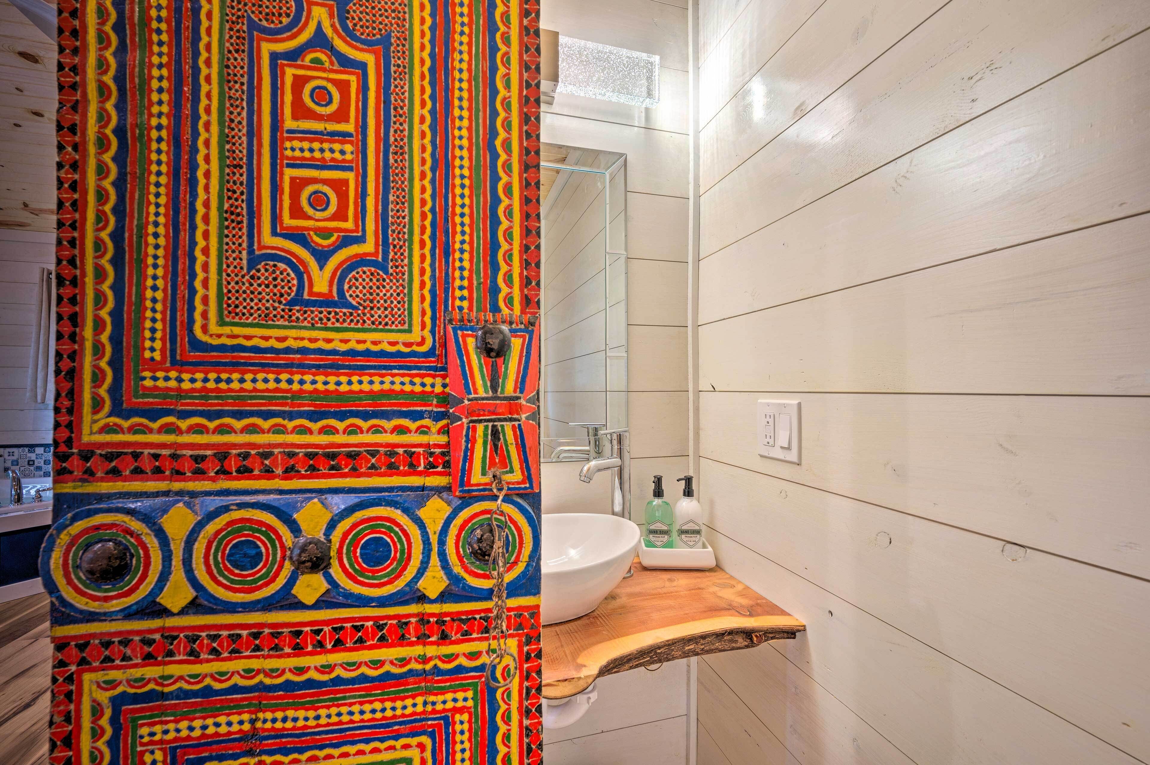 A bathroom with a colorful patterned door, a white sink, and a wooden countertop.