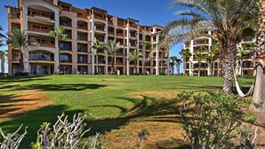 A multi-story hotel with balconies, palm trees, and a well-maintained lawn. - Paraiso del Mar Resort Condo: Water Taxi to La Paz (La Paz)