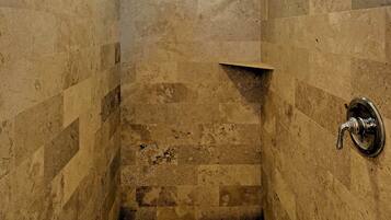 A small, tiled shower room with a window and a shelf.