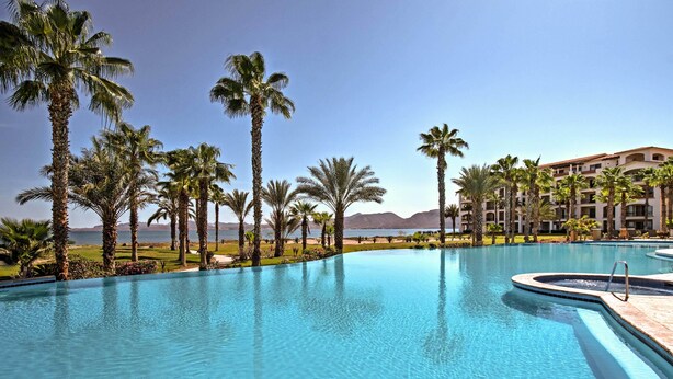 A swimming pool with palm trees and a view of the mountains. - Paraiso del Mar Resort Condo: Water Taxi to La Paz (La Paz)