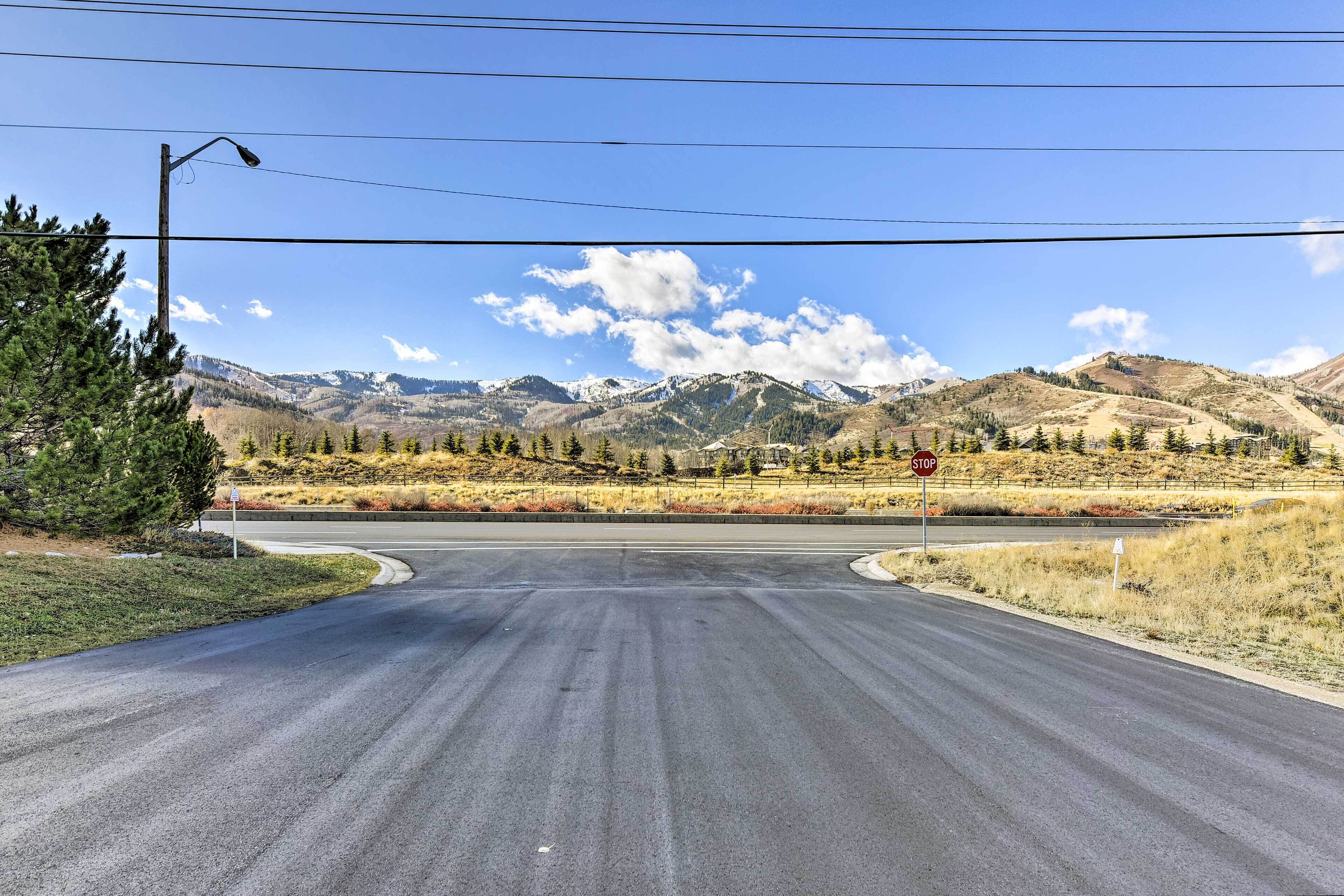 A road leading to a mountain range with a stop sign and a pedestrian crossing.