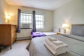 Una habitación de hotel con cama, mesita de noche, lámpara, cómoda y ventana con cortinas.