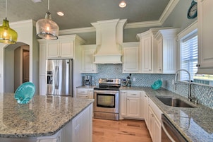 Una cocina con muebles blancos, encimeras de granito, electrodomésticos de acero inoxidable y una salpicadura trasera con azulejos azules.