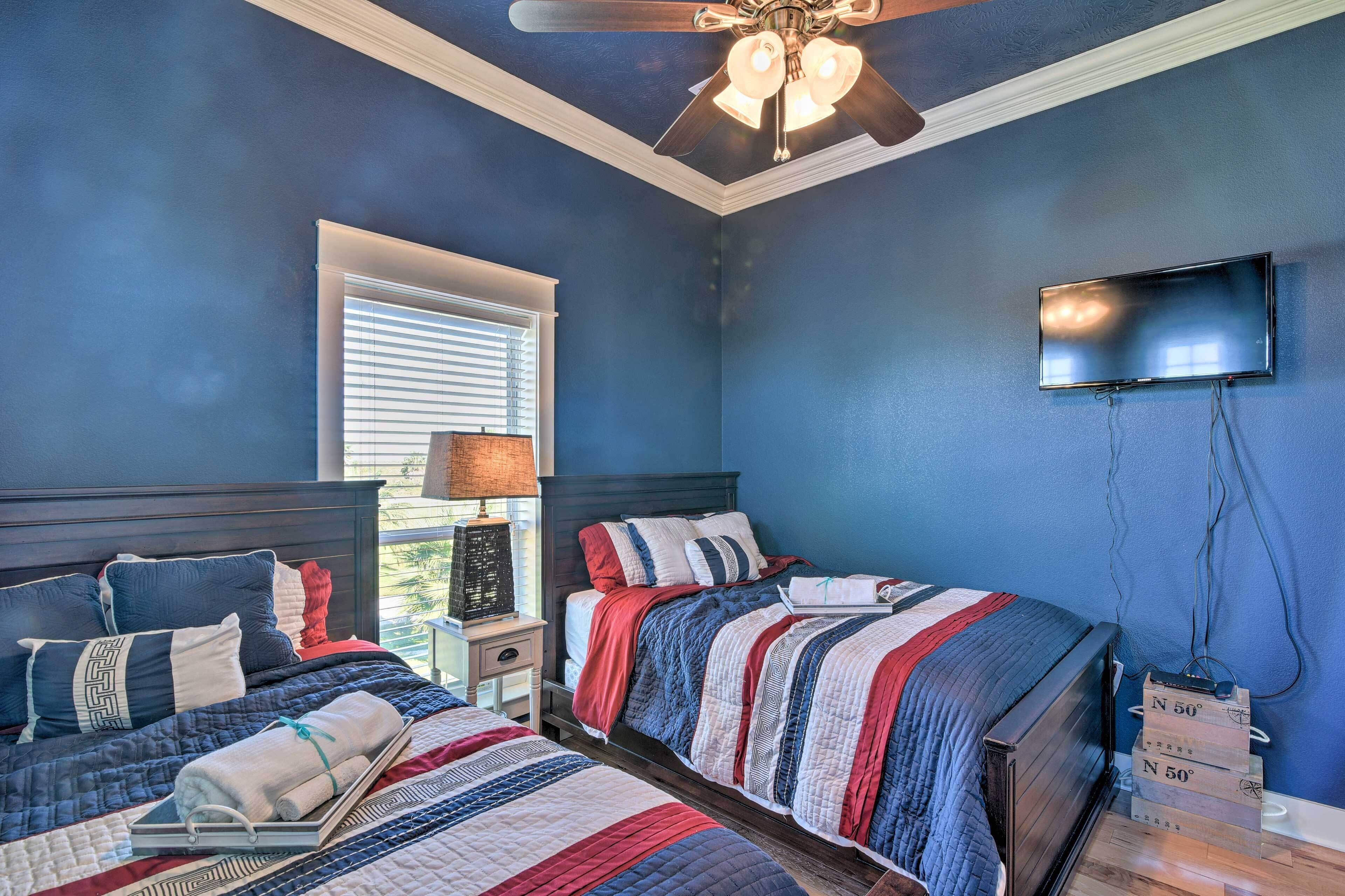 A bedroom with two beds, a ceiling fan, a TV, and a window with blinds.