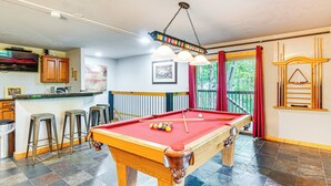 A pool table with a red felt top, surrounded by stools and a bar area with a countertop.